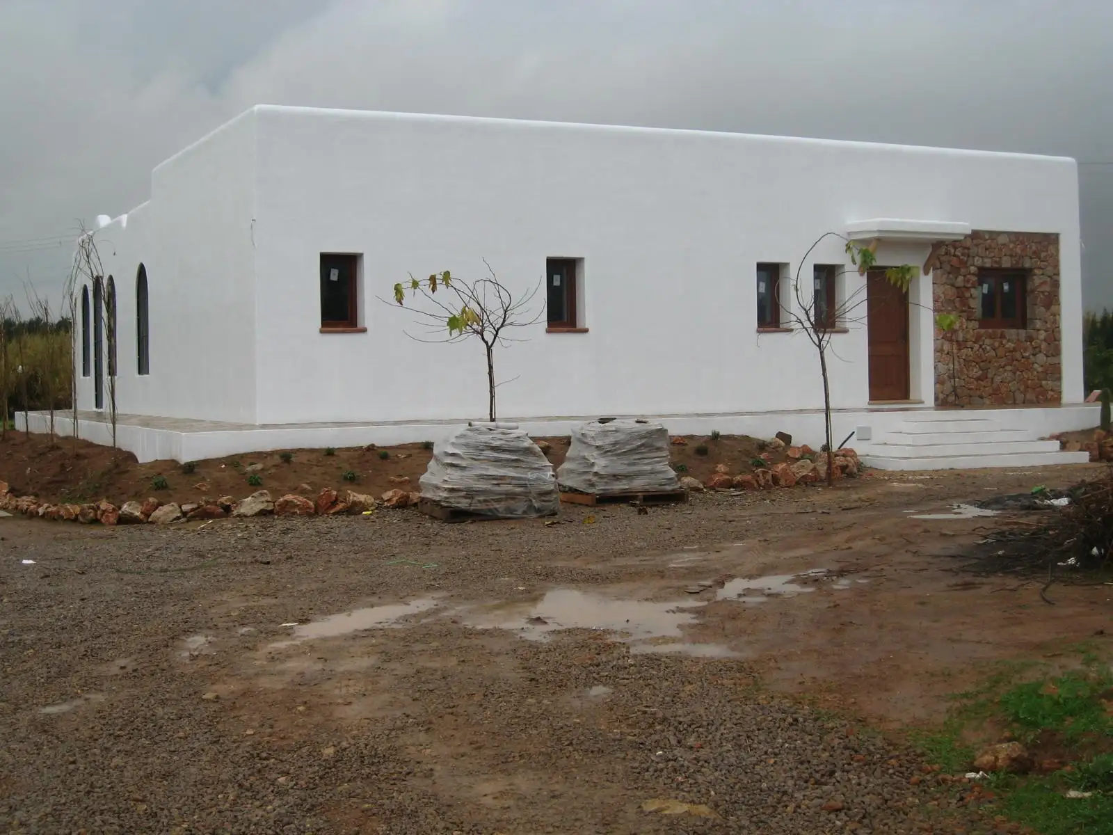 Rehabilitación de fachada blanca con zócalo de piedra y ventanas de madera en Ibiza