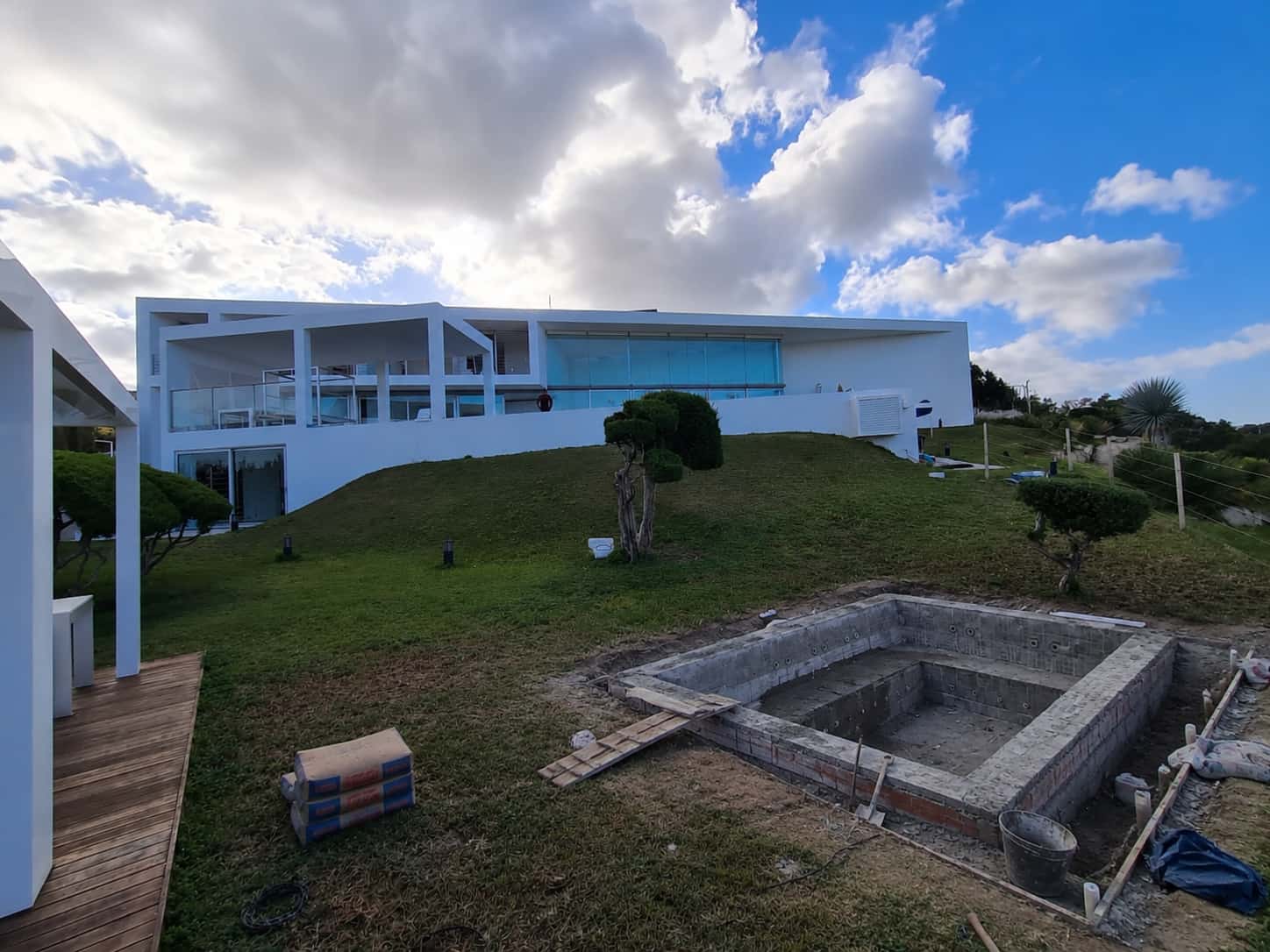 inicio de piscina con gresite azul y tarima de madera junto a fachada blanca en Ibiza