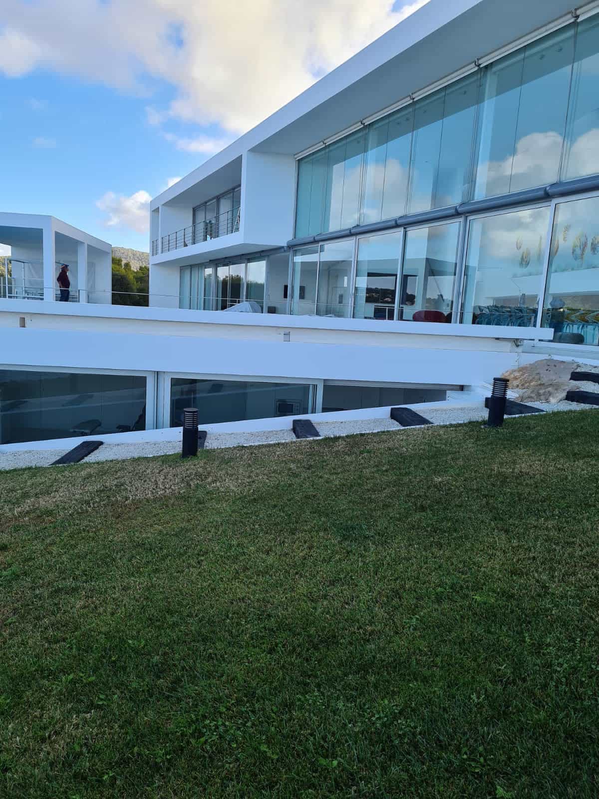 Rehabilitación de fachada minimalista con grandes ventanales de cristal y estructura blanca en Ibiza