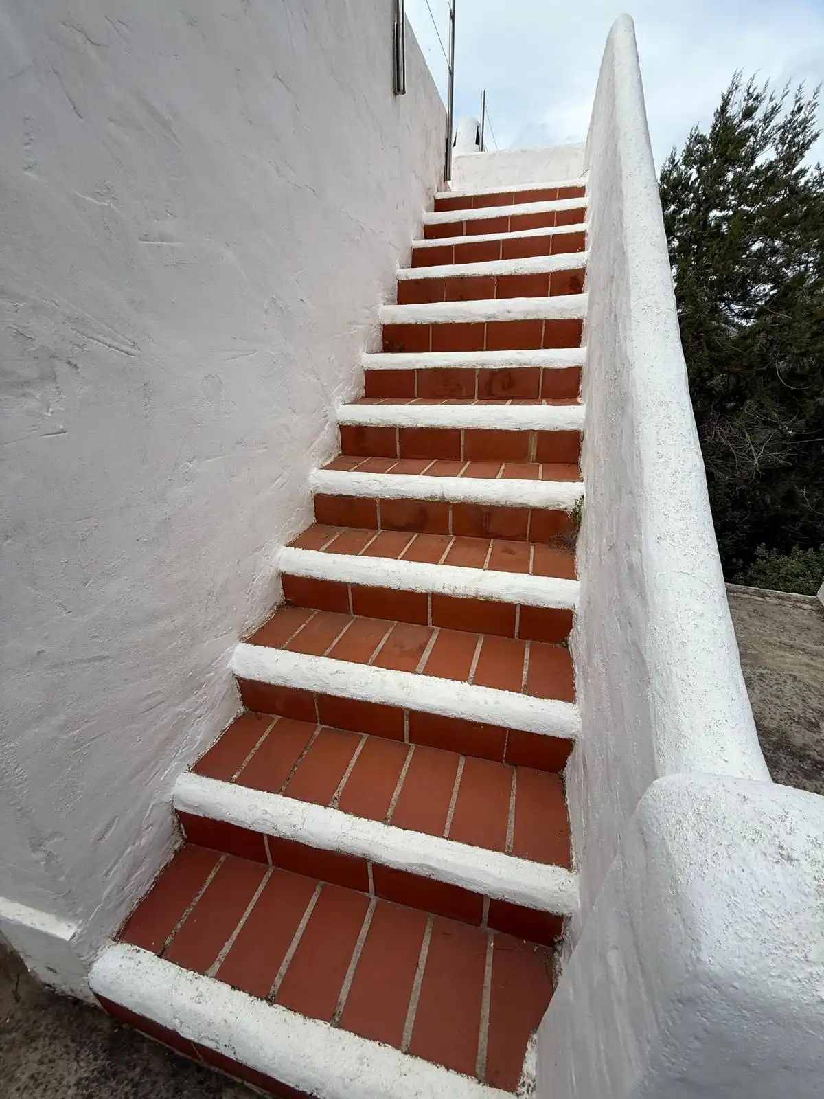Reforma de vivienda con escalera exterior de peldaños cerámicos y muros blancos encalados en Ibiza