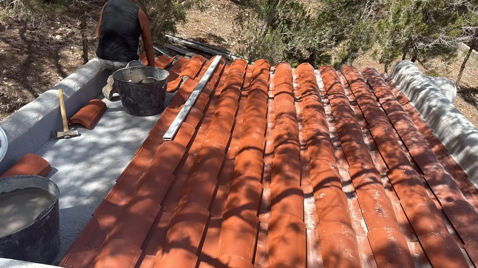Operario realizando una rehabilitación de tejado con tejas curvas de cerámica roja en Ibiza